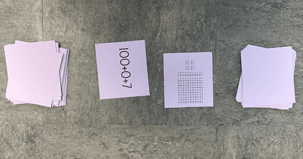 2 stacks of purple cards on the outside face down with 2 cards flipped up between with a number shown with base 10 blocks & a number shown in expanded form